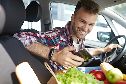 Portrait of smiling young man usiing smartphone in car with groceries, copy space