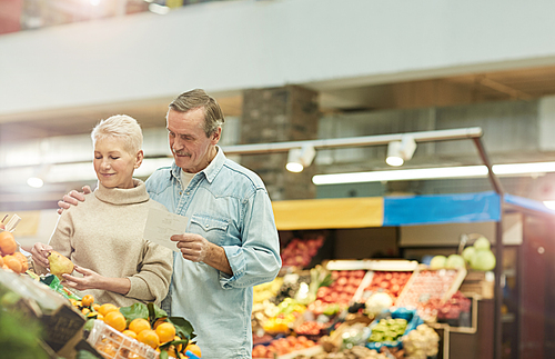 Waist up portrait of smiling senior couple choosing fruits while enjoying grocery shopping at farmers market, copy space