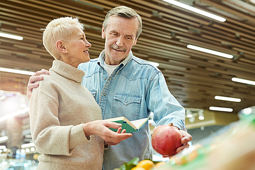 Waist up portrait of smiling senior couple choosing fresh fruits and vegetables while enjoying grocery shopping in supermarket, copy space