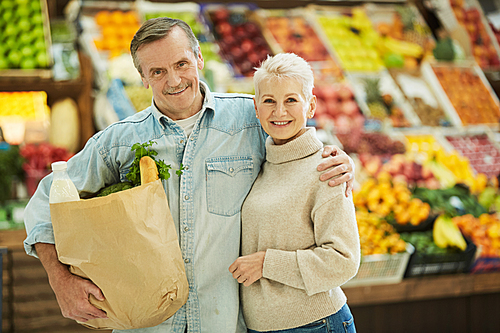 Waist up portrait of modern senior couple smiling at camera while enjoying grocery shopping at farmers market, copy space