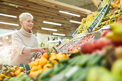 Waist up portrait of smiling adult woman choosing fresh vegetables while grocery shopping at farmers market, copy space