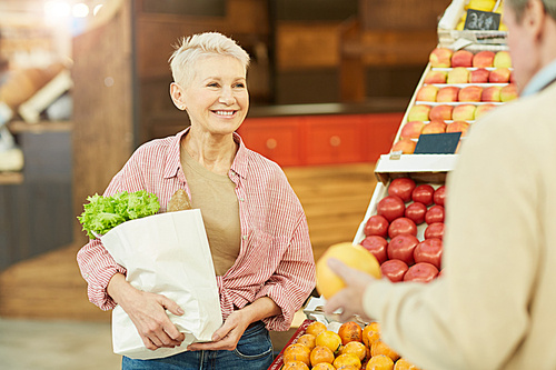 Waist up portrait of smiling mature woman enjoying grocery shopping at farmers market, copy space