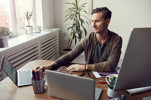 Portrait of handsome mature businessman using computers while multitasking at workplace in office, copy space