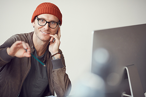 Portrait of contemporary man wearing glasses and beanie smiling at camera while posing at workplace in office, copy space
