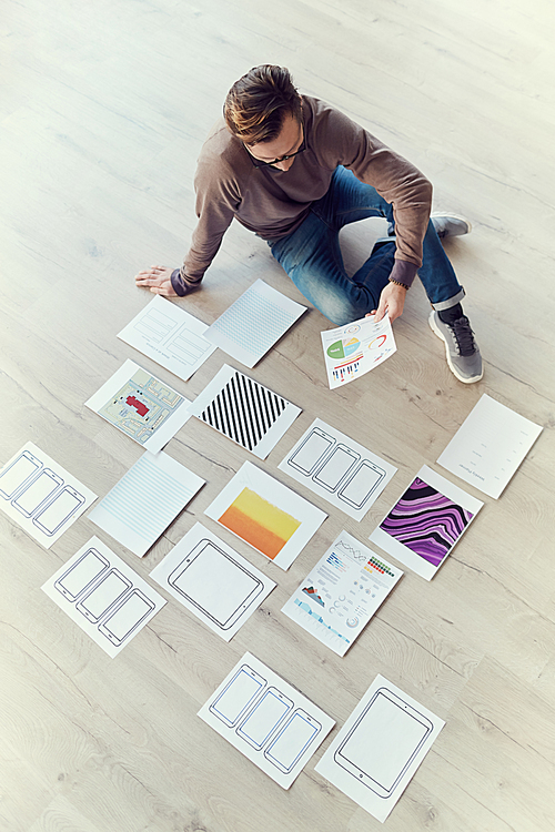 High angle portrait of contemporary businessman sitting on wooden floor in office and planning creative project laying out design patterns, copy space