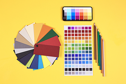 Top view flat lay of color palette samples and swatches laid out at designers workplace over pale yellow background, copy space