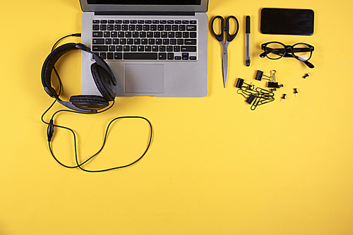 Above view of laptop computer and headphones at office workplace with pale yellow background, copy space
