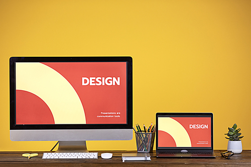 Designers workplace with two computer screens at wooden desk over pale yellow background, copy space