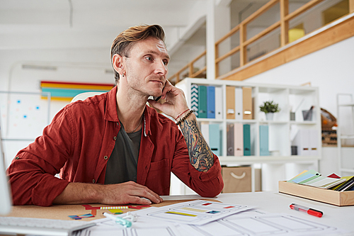 Portrait of contemporary adult man speaking by phone and looking away pensively while working at desk in office, copy space