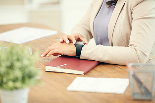 Close up of unrecognizable businesswoman checking smart watch while sitting at desk in office, copy space