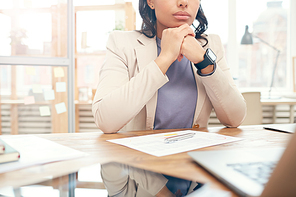 Cropped portrait of successful businesswoman looking away pensively while sitting at desk in office, copy space