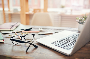 background image of business office with laptop and supplies on wooden desk, focus on  hard rim glasses in foreground, copy space