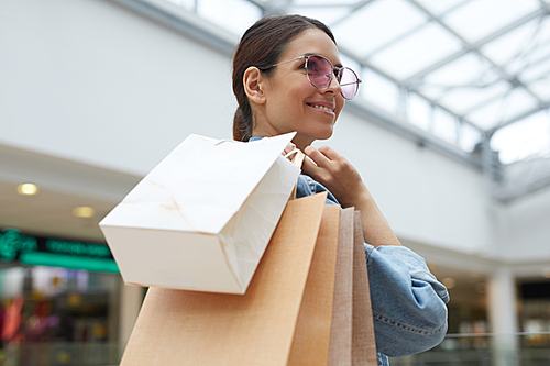 Young smiling girl in pink sunglasses and denim jacket enjoying shopping in new big shopping mall