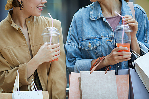 Close-up of young ladies with many paper bags drinking refreshing summer cocktails during shopping