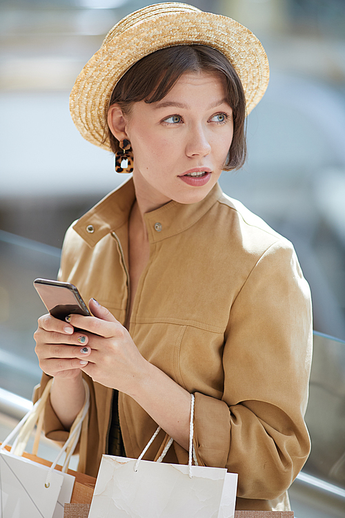 Content beautiful young woman with short hair wearing straw hat and beige jacket checking shopping promotions via mobile app