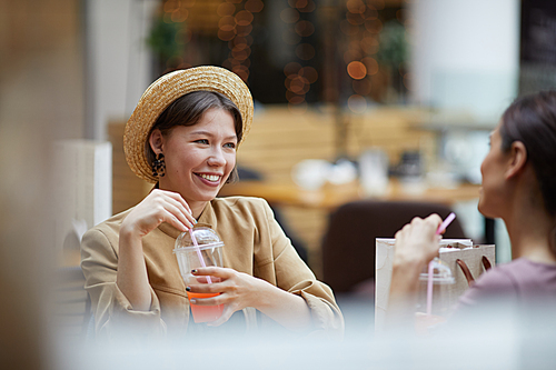 Happy attractive young women chatting about shopping and enjoying refreshing drinks in cafe