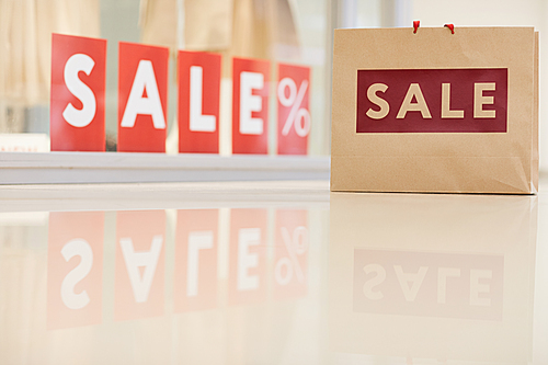 Background image of shopping bag standing against window display with red SALE sign, copy space