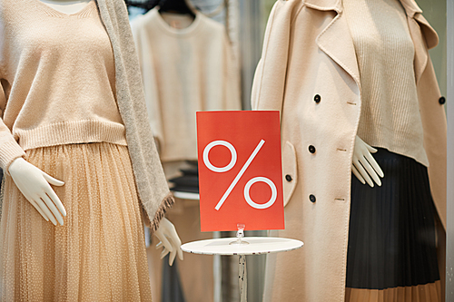 Close up of red SALE percent sign on window display with autumn clothes in shopping mall, copy space