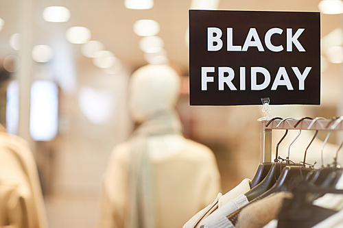 Close up background image of Black Friday sign on clothes rack with autumn clothes in shopping mall during sale season, copy space