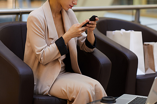 Mid-section portrait of elegant young woman using smartphone while relaxing in shopping mall, copy space