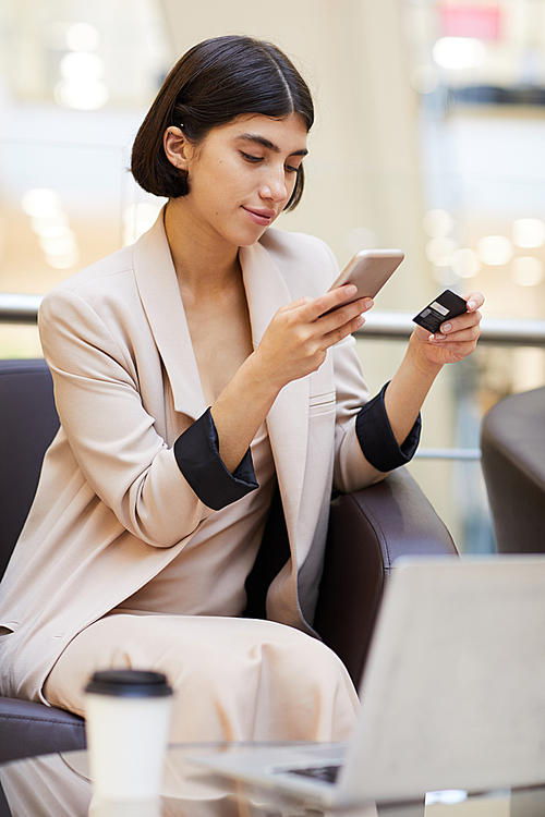 Portrait of elegant young woman holding credit card and smartphone while buying clothes online enjoying e-shopping
