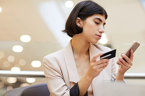 Portrait of elegant young woman holding credit card and smartphone while enjoying e-shopping, copy space