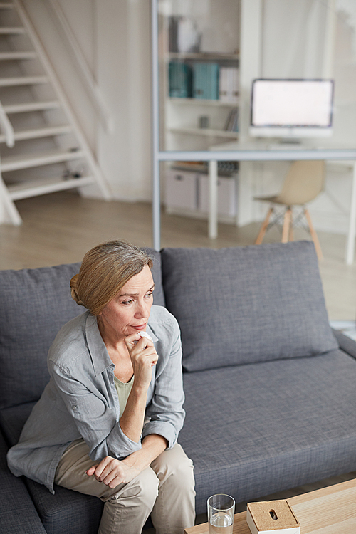 High angle portrait of sad mature woman sitting on couch at home and crying holding tissue, copy space