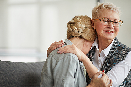 Portrait of caring female psychologist embracing senior patient while comforting her during therapy session, copy space