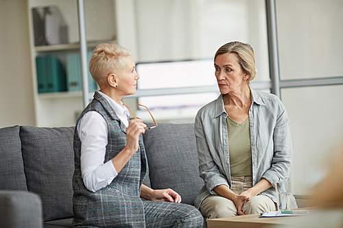 Portrait of mature woman looking at female psychologist while discussing mental issues during therapy session, copy space