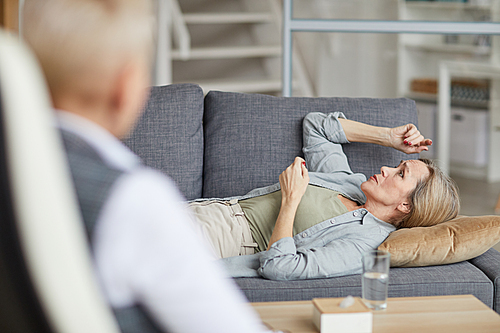 Side view portrait of crying mature woman lying on couch and talking to female psychologist during therapy session, copy space