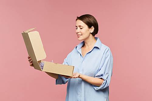 Happy young surprised woman opening box and looking at gift for holiday or her online order