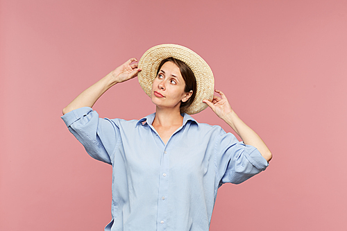 Young pretty woman in blue shirt trying new hat in isolation while going for summer vacation