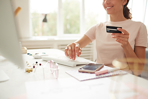 Close-up of positive young woman in tshirt sitting at table and adding credit card details on website while making online purchase