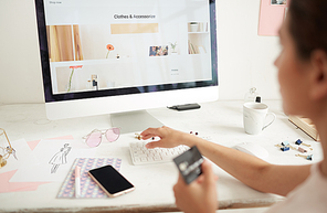 Close-up of woman sitting at table and buying clothing via online store using credit card, focus on computer screen