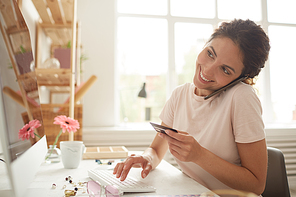 Cheerful attractive young woman sitting at table and asking helpdesk operator about online payment