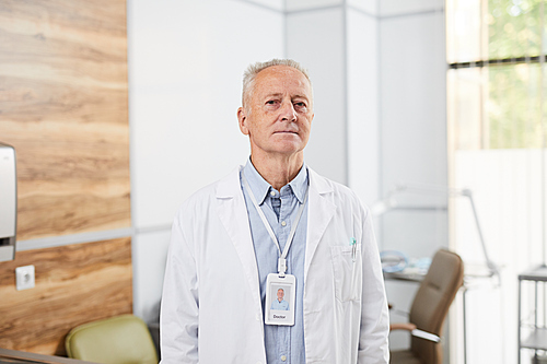Waist up portrait of senior doctor  while posing standing in office of modern clinic, copy space