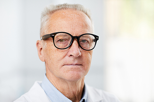 Head and shoulders portrait of white haired senior doctor wearing glasses and  while posing in office, copy space
