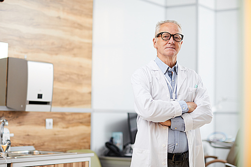 Portrait of confident senior doctor  while posing standing in office of modern clinic, copy space