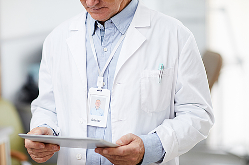 Mid section portrait of unrecognizable senior doctor holding digital tablet while standing in office of modern clinic and using internet, copy space