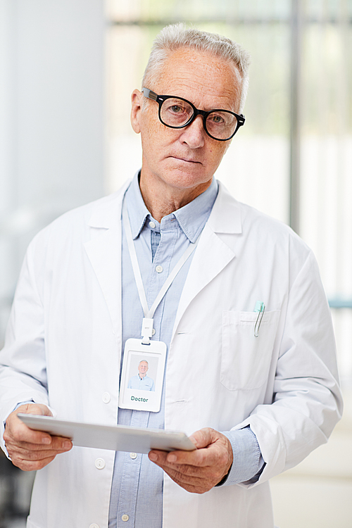 Waist up portrait of senior doctor  while using digital tablet standing in office of modern clinic