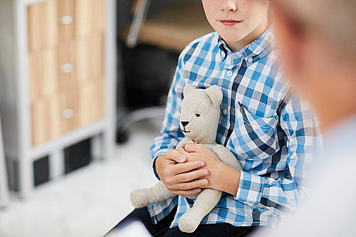 Close up of unrecognizable boy hugging bear toy while talking to doctor during consultation in child healthcare clinic, copy space