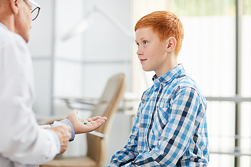 Portrait of smiling teenage boy looking at doctor during consultation in child clinic or hospital, copy space