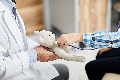 Closeup of little boy using stethoscope listening to heartbeat of plush bear during consultation with doctor in child clinic, copy space