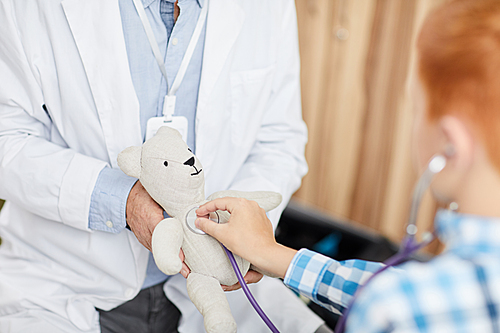 Close up of unrecognizable boy using stethoscope listening to heartbeat of plush bear during consultation with doctor in child clinic, copy space