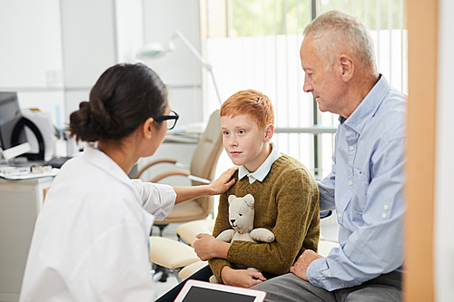 Back view portrait of caring nurse cheering up red haired boy during consultation in doctors office, copy space