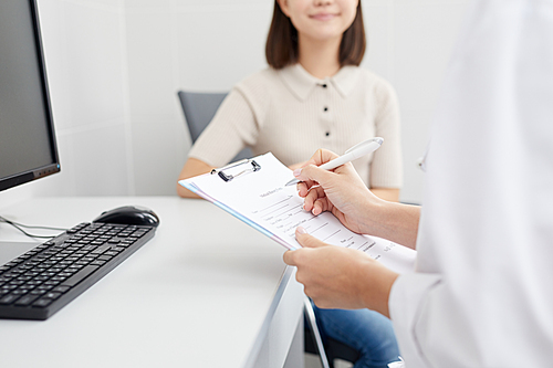 Closeup of unrecognizable doctor holding clipboard and filling patients form during consultation, copy space
