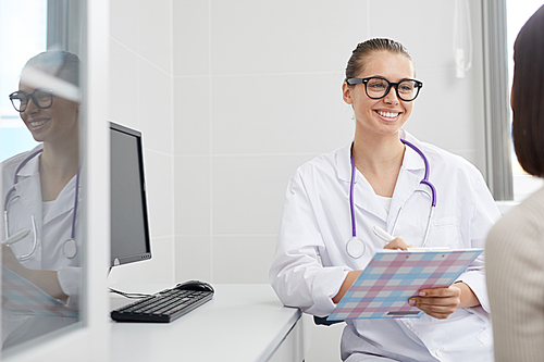 Portrait of young female doctor smiling happily while working with patient in clinic, copy space