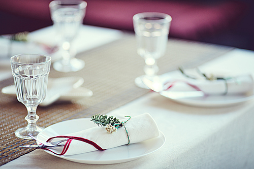 Close up of elegant table setting for Christmas dinner: white napkins tied with fir tree decor in violet interior, copy space