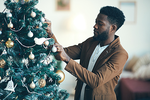 Waist up portrait of modern African-American man decorating Christmas tree at home, copy space