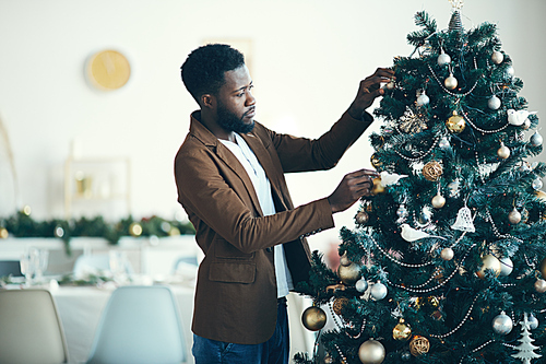 Side view portrait of young African-American man decorating Christmas tree at home, copy space
